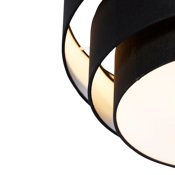 Nahaufnahme eines modernen Lampenschirms mit schwarzen Stoffspiralen und warm leuchtender Innenseite.