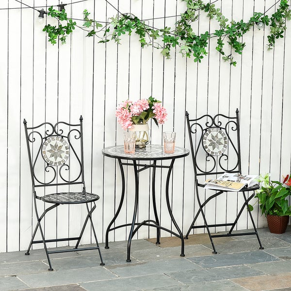 Bistro-Set aus Metall mit zwei Klappstühlen und einem runden Tisch mit Mosaikmuster vor einem weißen Holzzaun.