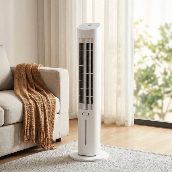 Weißer Turmventilator und Luftkühler in einem hellen Wohnzimmer neben einem hellen Sofa mit brauner Decke vor einem großen Fenster.