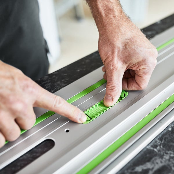 Hände eines Handwerkers beim Einstellen eines grünen Kunststoffschiebers an einer Festool Führungsschiene aus Aluminium.
