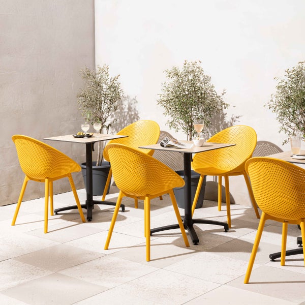 Moderne gelbe Gartenstühle aus Kunststoff mit Lochmuster und quadratische Bistrotische mit Holzoptik-Platte auf einer sonnigen Terrasse.