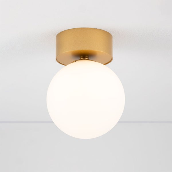 Goldene Deckenleuchte mit runder, opaler Glaskugel.