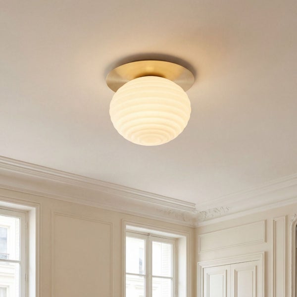 Deckenleuchte mit geriffeltem Glasschirm und Messinghalterung in einem hellen Raum mit klassischen Stuckverzierungen.