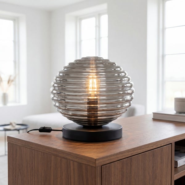Moderne Tischleuchte mit kugelförmigem Schirm aus geriffeltem Glas auf einem Holzmöbel in einem hellen Raum.