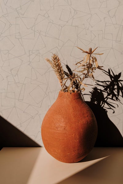 Tonvase mit getrockneten Blumen vor einer Tapete mit geometrischem Muster