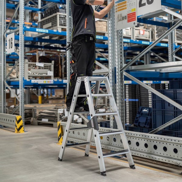 Eine Person steht auf einer Stufenleiter und befestigt ein Schild in einem Lagerregal.