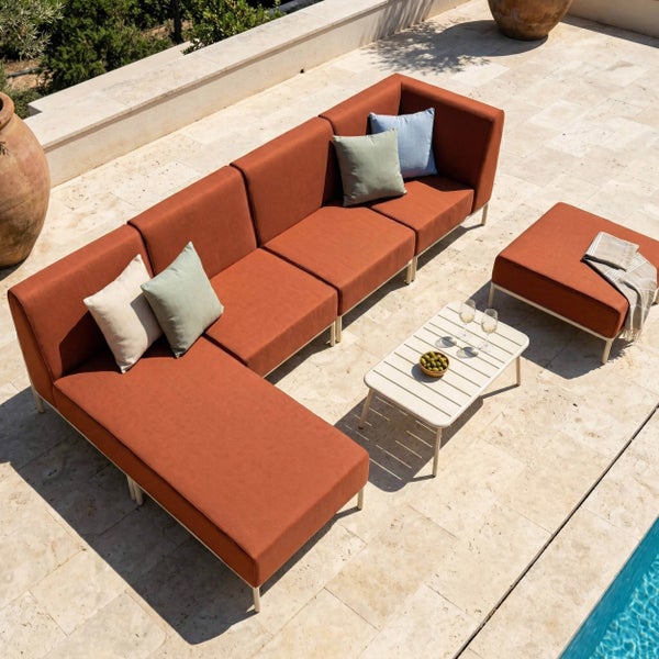 Modulare Outdoor-Lounge in Terracotta mit Sofa-Ecke, Récamiere, Hocker und weißem Lattentisch auf einer hellen Steinterrasse neben einem Pool.