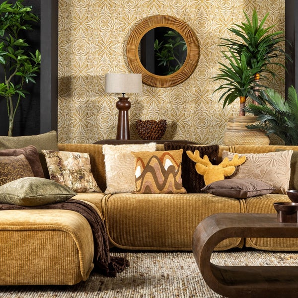 Wohnzimmer mit einem Cordsofa, gemusterter Tapete, rundem Spiegel, Lampen und Zimmerpflanzen in einem organisch gestalteten Interieur.