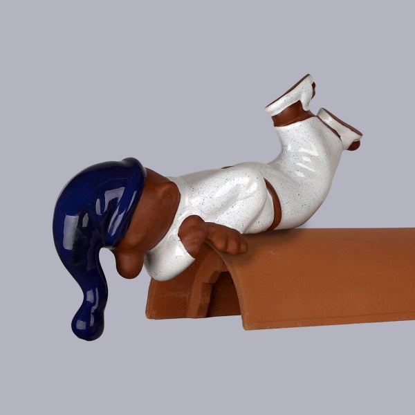 Dachschmuck Schlafwandler aus Keramik mit blauem Hut, liegend auf einem Firstziegel.