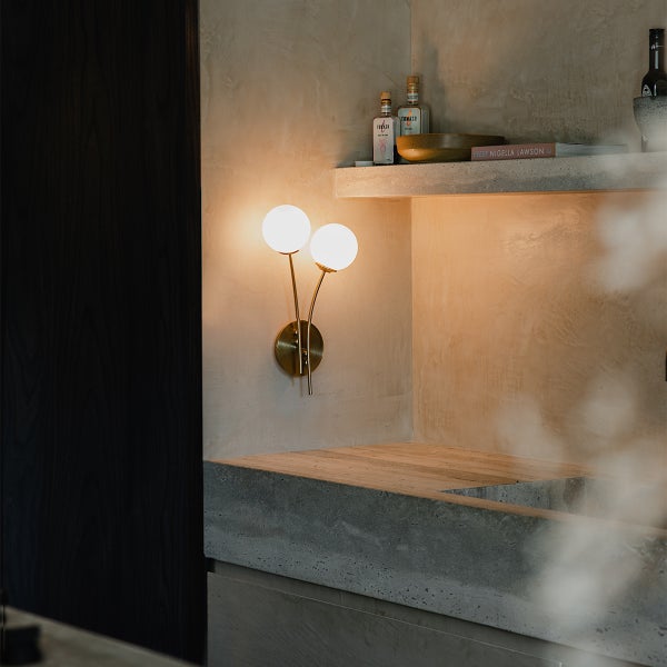 Wandleuchte mit zwei kugelförmigen Lampen an goldenem Gestell in einem hellen Raum.