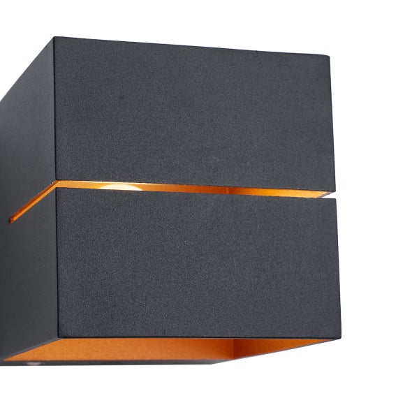Moderne würfelförmige Wandleuchte in Anthrazit mit goldenem Lichtschlitz und warmem Lichteffekt.
