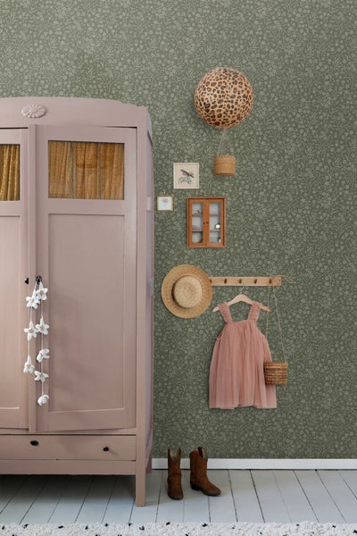 Dunkelgrüne Tapete mit floralem Muster, vintage rosa Holzschrank, Strohhut und Kleid an einer Hakenleiste in einem ordentlichen Kinderzimmer.