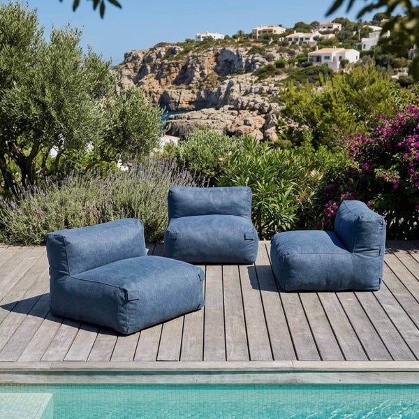 Drei blaue Outdoor-Sitzsäcke auf einer Holzterrasse am Pool mit Blick auf eine Küstenlandschaft mit Vegetation und Gebäuden.