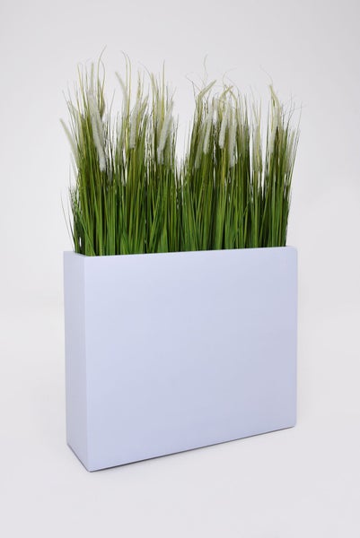 Künstliches Gras in einem rechteckigen weißen Pflanzgefäß als dekorativer Sichtschutz für Innenräume.