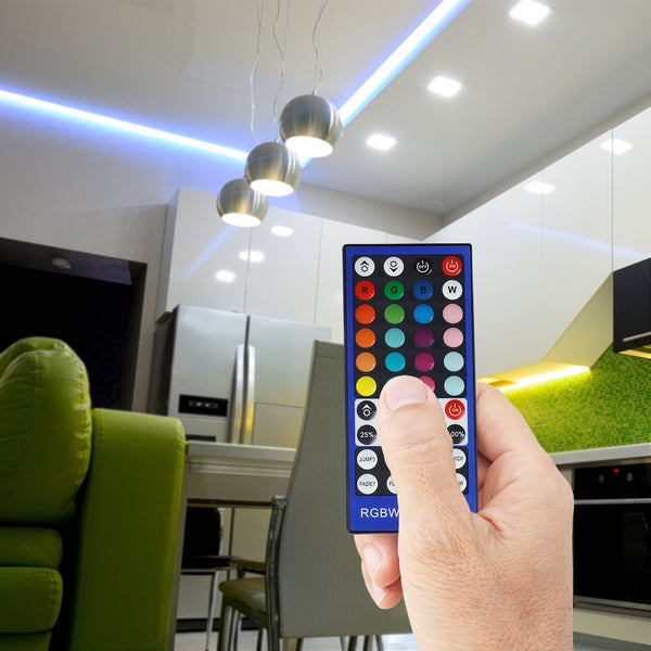 Hand mit Fernbedienung zur Steuerung der Beleuchtung in einem modernen Wohnraum.