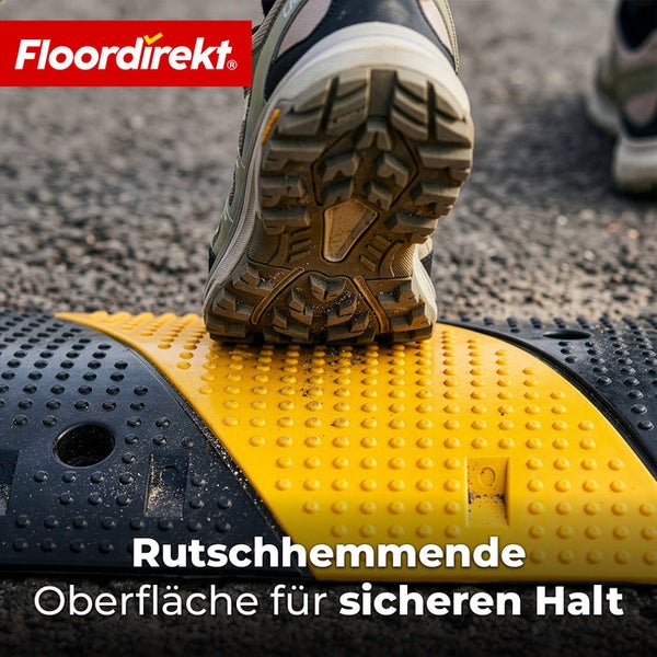 Ein Schuh mit Profilsohle steht auf einer gelb-schwarzen Fahrbahnschwelle mit rutschhemmender Noppenstruktur. Floordirekt Logo.