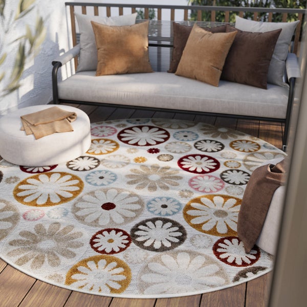 Runder Outdoor-Teppich mit buntem Blumenmuster auf einer hellen Holzterrasse mit modernem Sofa und Pouf.