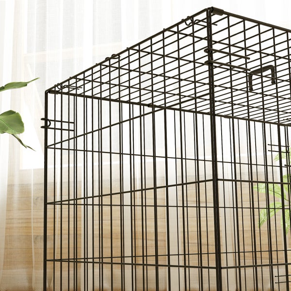 Nahaufnahme eines schwarzen Gitterkäfigs aus Metall für Haustiere in einem hellen, organisierten Zimmer mit Pflanzen.
