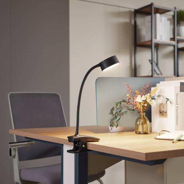 Schwarze LED-Klemmlampe mit flexiblem Hals an einem Schreibtisch aus Holz in einem hellen, organisierten Arbeitszimmer.