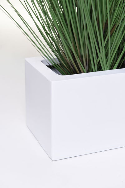 Künstliches Gras in einem weißen quadratischen Pflanzgefäß.