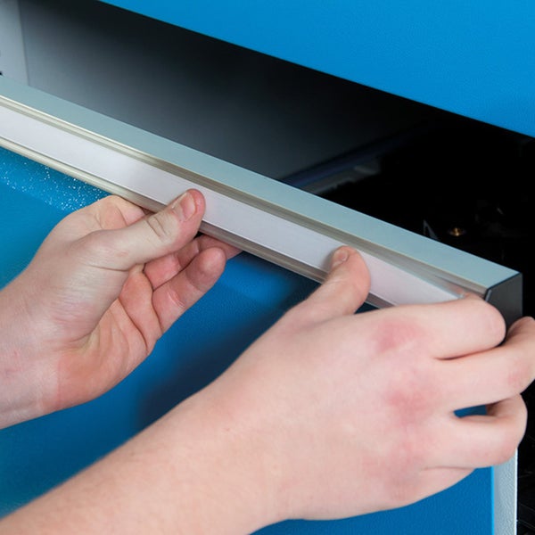 Hände setzen einen weißen Beschriftungsstreifen in den Metallgriff einer blauen Werkzeugschrankschublade ein.