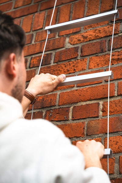 Person klettert an einer Rettungsleiter mit Aluminiumsprossen und Stahlseilen an einer Ziegelwand.