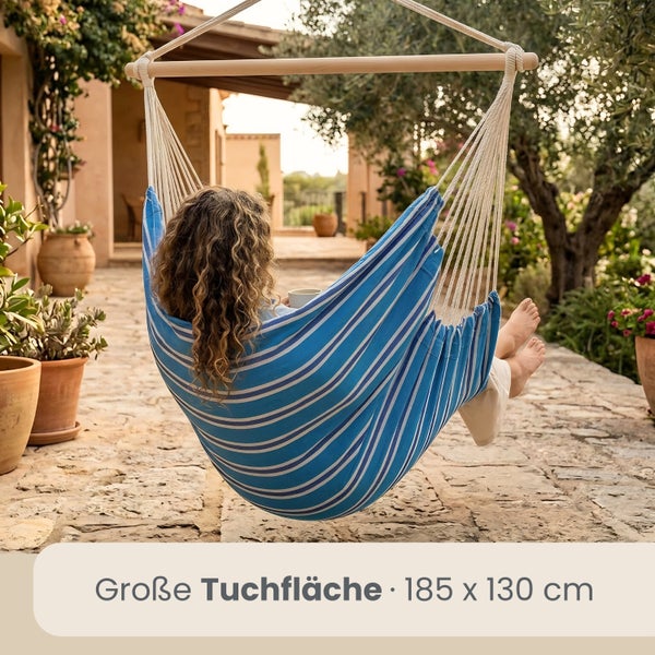 Person sitzt in einem Hängesessel mit blau-weiß gestreifter Tuchfläche von 185 mal 130 Zentimetern auf einer gepflasterten Terrasse im Garten.