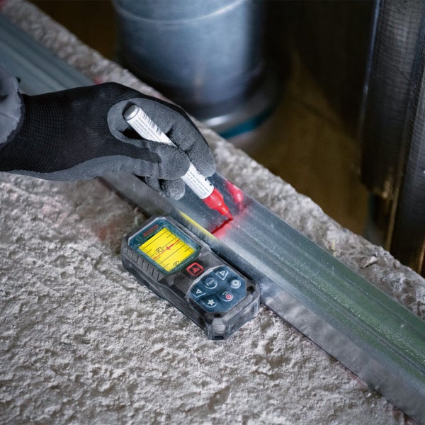 Ein Bauarbeiter mit Schutzhelm verwendet einen Laser-Entfernungsmesser an einer Wand