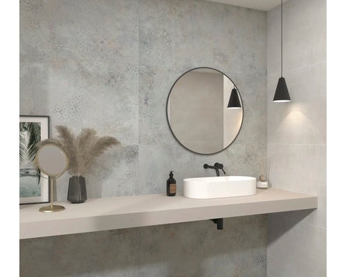 Modernes Badezimmer mit grauen Wandfliesen in Betonoptik und dezentem Muster, weißem Aufsatzwaschbecken auf hellem Waschtisch und rundem Spiegel.