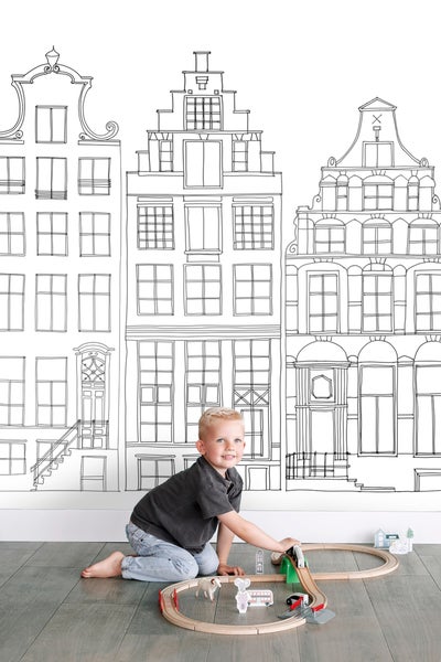 Junge spielt mit Holzeisenbahn vor einer Wand mit Hauszeichnung