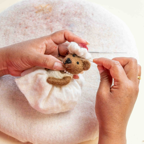 Hände, die einen Teddybären mit Nadel und Faden nähen
