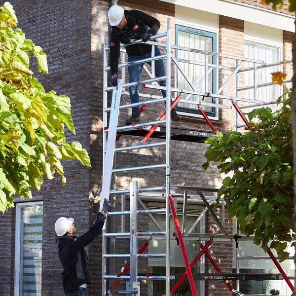 Zwei Handwerker bauen ein Altrex Rollgerüst vor einem Haus auf.
