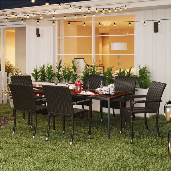 Gartensitzgruppe mit Holztisch und sechs dunklen Polyrattan-Sesseln auf einer Rasenfläche, dekoriert mit einer Lichterkette und Pflanzen.