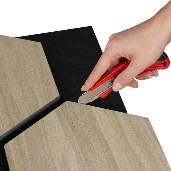 Hand schneidet ein hexagonales Wandpaneel in Holzoptik mit einem Cuttermesser zu.