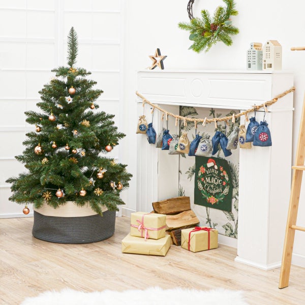 Weihnachtliche Wohnzimmerdekoration mit einem geschmückten Tannenbaum im Korb, einem Kamin mit Adventskalender aus Stoffbeuteln und Geschenkpaketen.