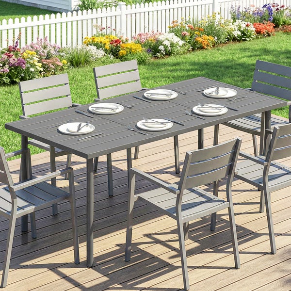 Eine Frau sitzt an einem verzierten Metall-Bistrosset auf einer hellen Holzterrasse. Dekorative Gartenmöbel aus Metall mit Gartenblick.