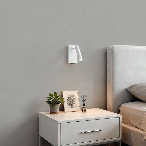 Weiße LED-Wandleuchte montiert über einem weißen Nachttisch in einem modern eingerichteten Schlafzimmer mit Bett und Dekoration.