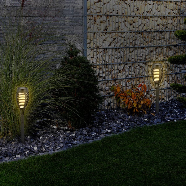 Szene mit zwei Gartenfackeln zwischen Pflanzen und Steinen