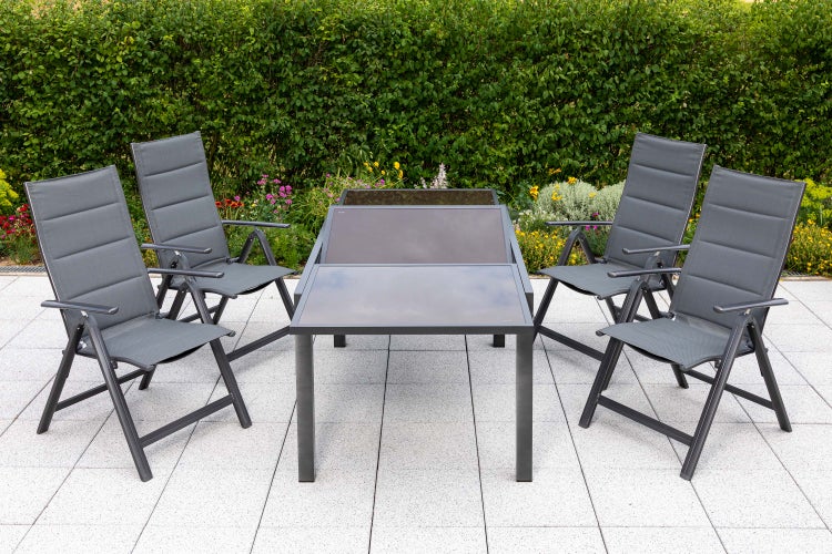 Gartensitzgruppe mit vier Stühlen und Tisch mit Glasplatte vor Hecke