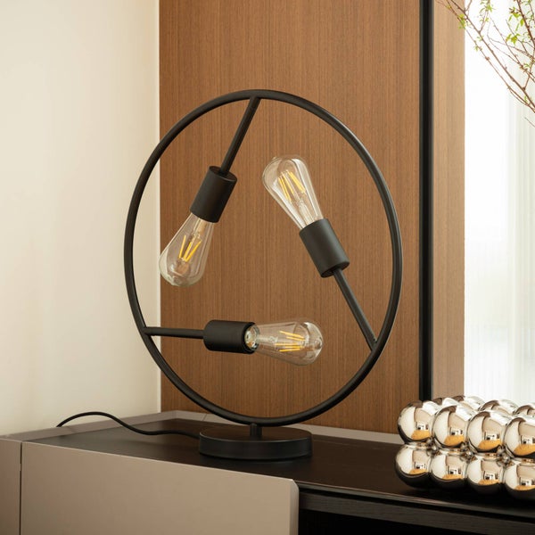 Dekorative Tischleuchte mit drei Glühbirnen in einem kreisförmigen, schwarzen Metallrahmen.