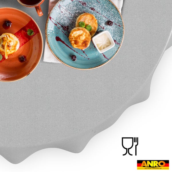 Hellgraue, fein strukturierte Tischdecke auf einem runden Tisch mit Frühstücksgeschirr. Symbol für Lebensmittelechtheit und ANRO Logo.