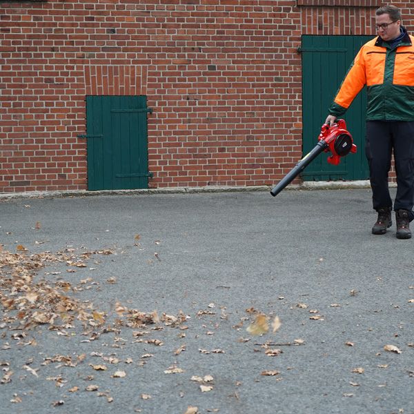 Eine Person verwendet einen Laubbläser zur Reinigung eines Hofs.