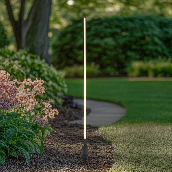 Schlanke, vertikale LED-Gartenleuchte mit Erdspieß in einem Beet neben einer Rasenfläche.