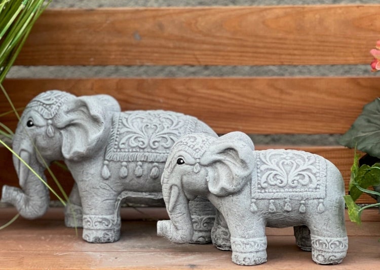 Zwei graue Gartenfiguren in Elefantenform mit verzierten Mustern aus Stein auf einer Holzfläche.