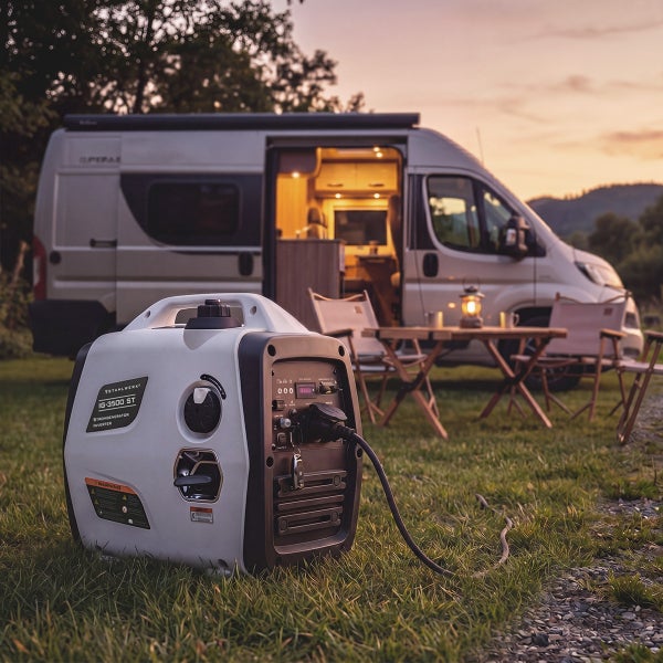 Tragbarer Inverter Stromerzeuger vor einem Wohnmobil beim Camping in der Natur bei Sonnenuntergang.