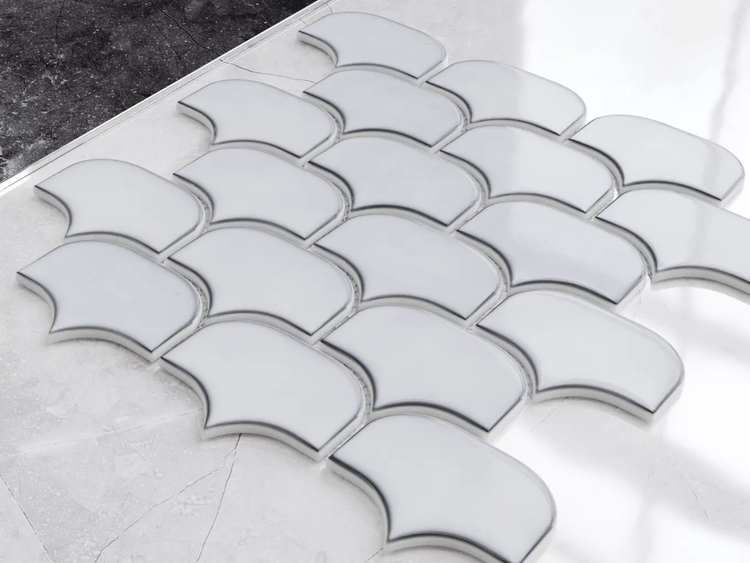Weiße Mosaikfliesen in Fischschuppen-Form mit glänzender Oberfläche auf hellem Marmor in einer hellen, modernen Szene.
