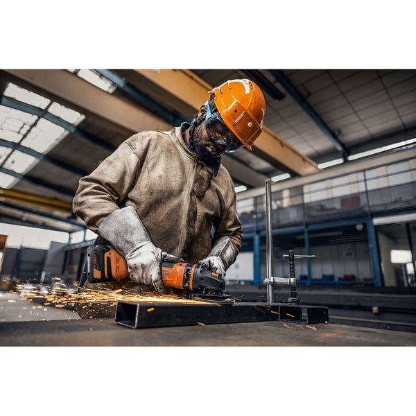 Person in Schutzkleidung bearbeitet Metall mit einem orangefarbenen Akku-Winkelschleifer, Funkenflug bei der Arbeit in einer Werkstatt.