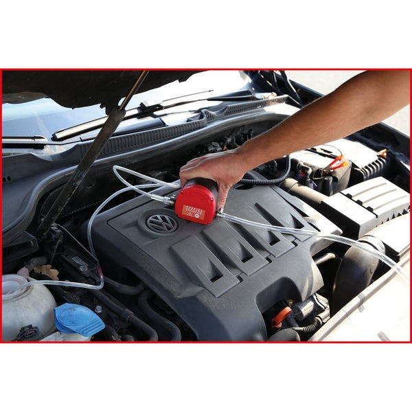 Eine Hand hält eine Absaugpumpe, die an einem Automotor angeschlossen ist, zum Ölwechsel.