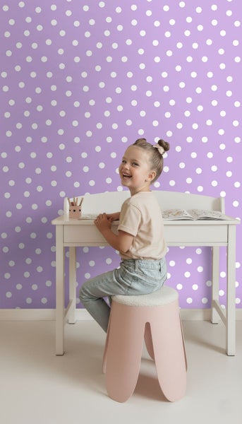 Mädchen sitzt an einem Schreibtisch vor einer Tapete mit Punktmuster
