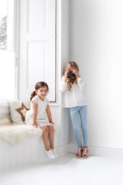 Zwei Mädchen in einem hellen, organisierten Raum: eines mit einer Kamera, das andere in einem Kleid.